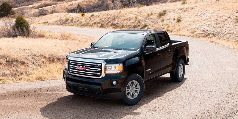 a black 2020 gmc canyon truck driving in the dessert on a paved road