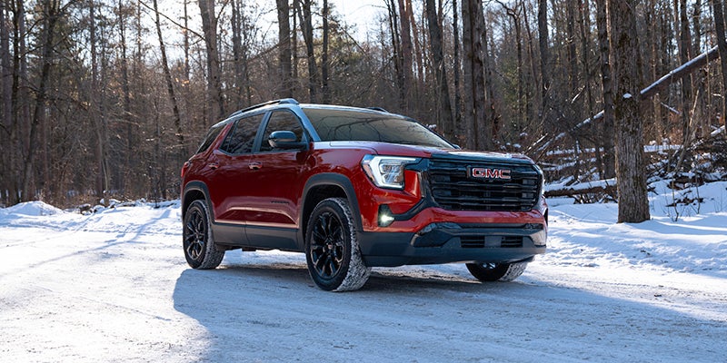 a red 2025 gmc terrain parked in the woods with snow on the ground