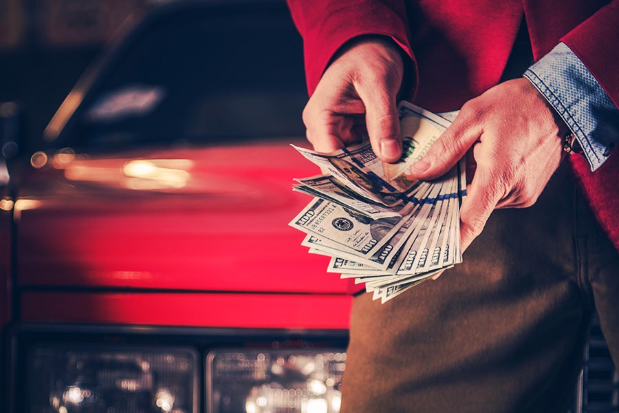 a person with money in their hands with a red car in the background